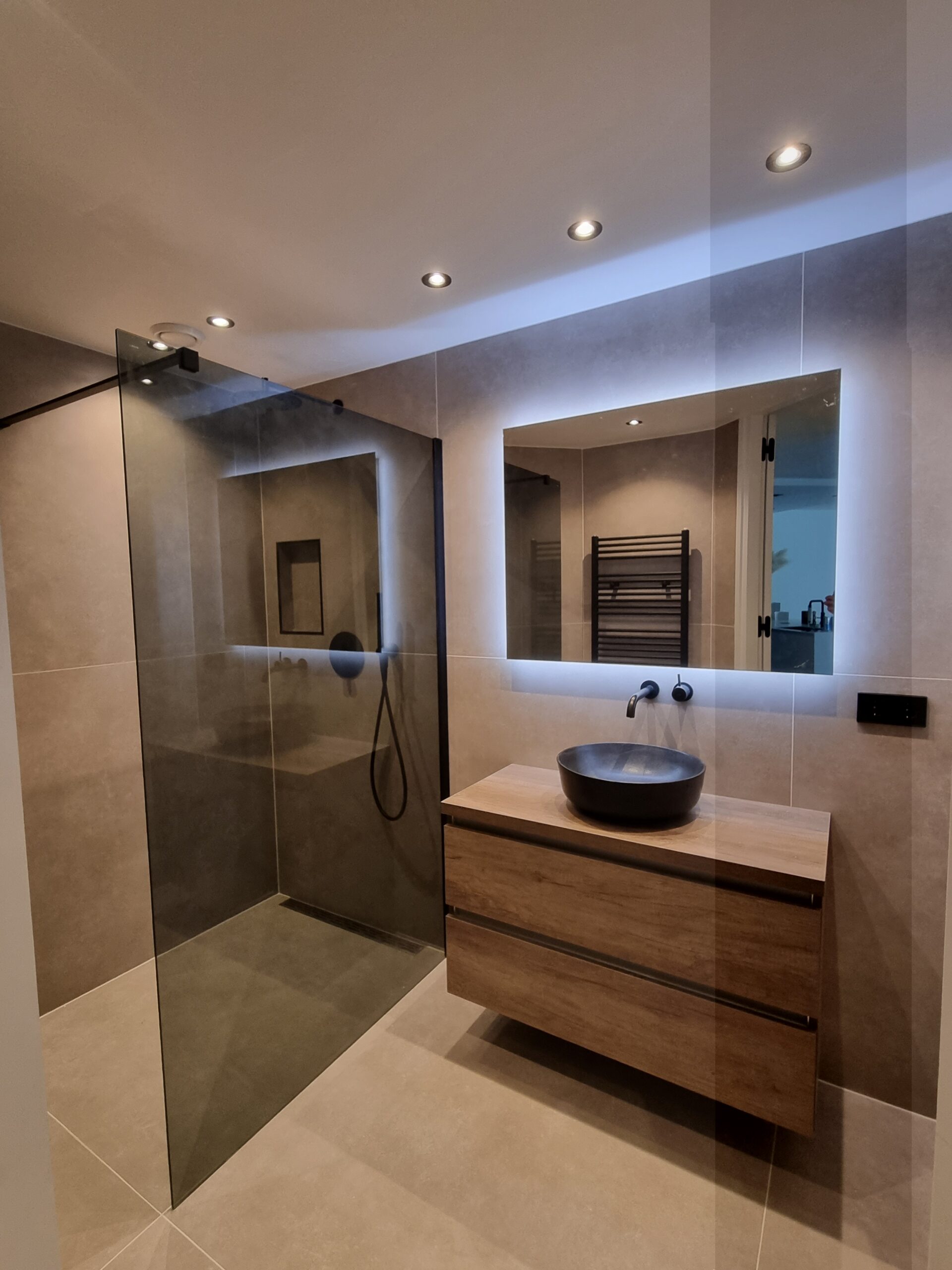 Badkamer inspiratie: grote tegels, inloopdouche, verlichte spiegel en inbouw spots.